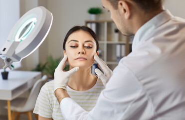 Woman preparing for plastic surgery, being examined by plastic surgeon in clinic under lamp. Female...