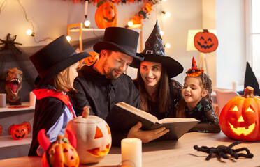 Happy family of four members celebrating Halloween together, reading mysterious book and telling...