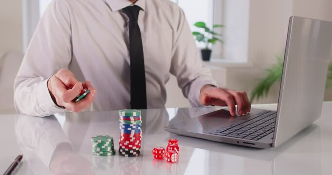 Excited overjoyed man at computer desk holding online casino poker chips, jetons, winner feeling euphoric with bet gambling victory, looks at screen celebrates fantastic news, received best prize