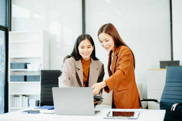  Asian businesswomen collaborate on tablet and laptop in a modern office, discussing strategy and...