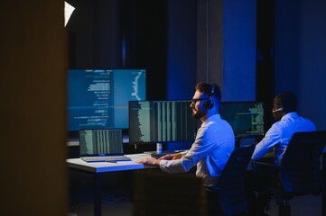 Male Data Scientist Works on Personal Computer Wearing a Headset in Big Infrastructure Control and...