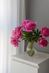 large pink peonies in a glass vase on a nightstand in the interior