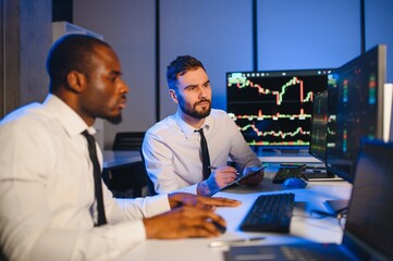 Fototapeta na wymiar Two businessmen, financial analysts or investment advisers sitting at office desk with copmputers and documents