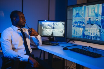 African-American security officer watching the screens talking on radio in control room
