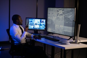 African American security officer or dispatch uses computer and walkie talkie, looks at screens