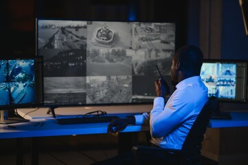 African-American security officer watching the screens talking on radio in control room