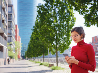 Fototapeta premium Beautiful woman in walking in Frankfurt on spring day and holding mobile phone. Urban lifestyle concept. Check social networks, send sms or book hotel, exuding confidence and professionalism