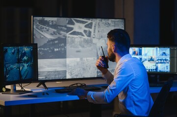 Back view of man watching surveillance footage and map on computers