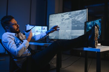 Male Security Guard Talking On Walkie talkie While Monitoring Multiple CCTV Footage On Computer