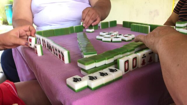 Family members are spending time playing the game of mahjong together at the table