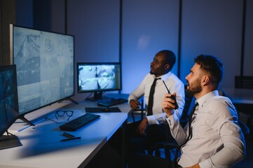 Two male security guards looking at computer screen while one of them explaining detail of video