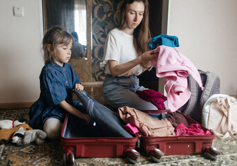 Tired mother with 6 year old daughter packing travel suitcase. Travel concept. Close-up of travel bag and tired faces of travelers.