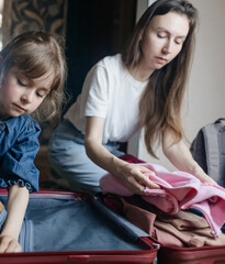Tired mother with 6 year old daughter packing travel suitcase. Travel concept. Close-up of travel bag and tired faces of travelers.