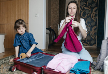 Tired mother with 6 year old daughter packing travel suitcase. Travel concept. Close-up of travel bag and tired faces of travelers.