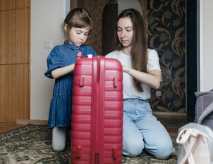 Tired mother with 6 year old daughter packing travel suitcase. Travel concept. Close-up of travel bag and tired faces of travelers.
