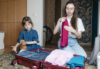 Tired mother with 6 year old daughter packing travel suitcase. Travel concept. Close-up of travel bag and tired faces of travelers.
