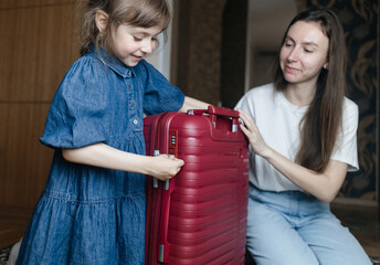 Tired mother with 6 year old daughter packing travel suitcase. Travel concept. Close-up of travel bag and tired faces of travelers.