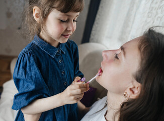 Daughter puts makeup on her mother face and plays around. Caring parent allows her child to paint her face. Happy childhood. Concept of loving family and fun. little girl doing her makeup