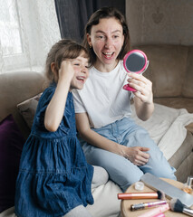 Daughter puts makeup on her mother face and plays around. Caring parent allows her child to paint her face. Happy childhood. Concept of loving family and fun. little girl doing her makeup