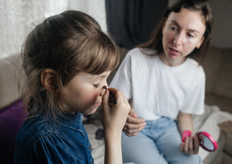 Daughter puts makeup on her mother face and plays around. Caring parent allows her child to paint her face. Happy childhood. Concept of loving family and fun. little girl doing her makeup