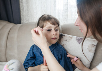 Mother putting makeup on her daughter face and they fool around together. Communication between women in the family. Fun time. Happy family concept. little girl doing her makeup