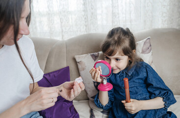 Mother putting makeup on her daughter face and they fool around together. Communication between women in the family. Fun time. Happy family concept. little girl doing her makeup