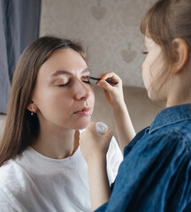 Daughter puts makeup on her mother face and plays around. Caring parent allows her child to paint her face. Happy childhood. Concept of loving family and fun. little girl doing her makeup