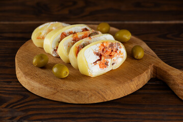 Slices of farm cheese roll with salmon, olives and cream cheese on wooden board. Healthy rustic breakfast.
