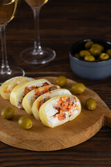Slices of farm cheese with salmon, olives and cream cheese on a brown wooden board with white non-alcoholic wine. Healthy rustic breakfast. Vertical orientation.