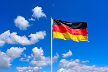 The flag of  Germany flutters in the wind in a blue sky with white clouds