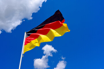 The flag of  Germany flutters in the wind in a blue sky with white clouds