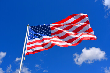 Fototapeta premium The flag of United States flutters in the wind in a blue sky with white clouds