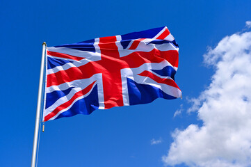 The flag of United Kingdom  flutters in the wind in a blue sky with white clouds