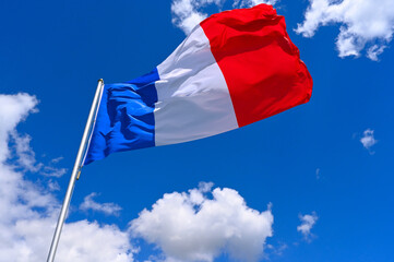 The flag of  France flutters in the wind in a blue sky with white clouds