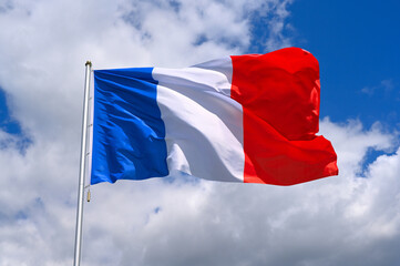 The flag of  France flutters in the wind in a blue sky with white clouds