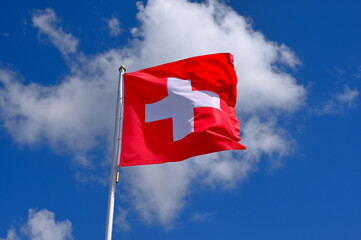 flag of Switzerland fluttering in the blue sky with cumulus clouds
