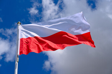 The flag of  Poland flutters in the wind in a blue sky with white clouds
