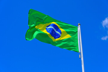 The flag of Brazil flutters in the wind in a blue sky