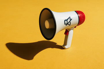Fototapeta premium A white and red megaphone with a mute icon casts a shadow on a vibrant yellow background.