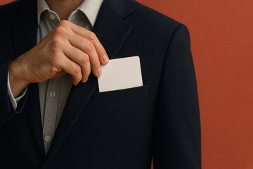 A man in a suit places a blank business card into his jacket pocket against a red background.