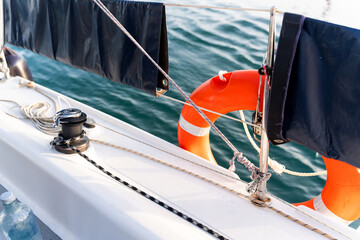 Sailing boat deck with winch, ropes, and lifebuoy navigating calm waters