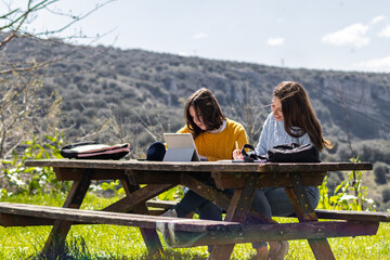 University students studying outdoors on a wooden table with tablet and notebooks