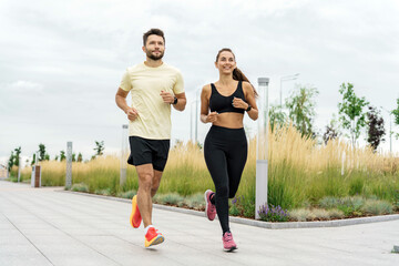 Couple enjoying a joyful morning run through a scenic park lined with tall grass and modern pathways