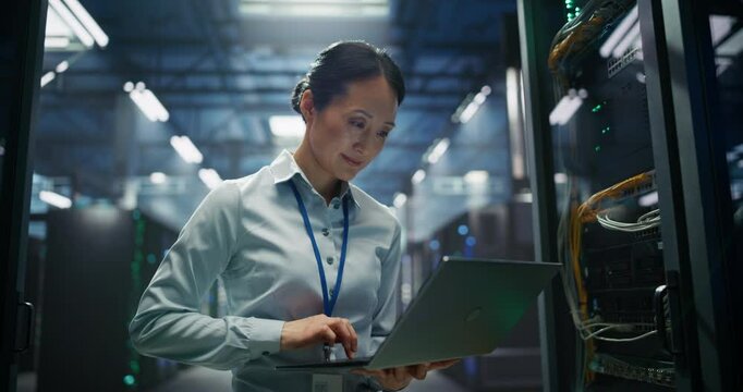 Female Data Center Administrator Using Laptop Computer. Asian Maintenance Specialist Working on Cyber Security and Network Protection in AI Computing Facility. Engineer Checking Server Farm Analytics
