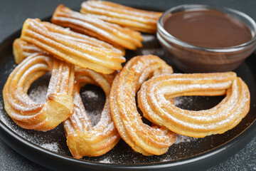 Traditional spanish dessert churros, fried dough pastry dusted with powdered sugar and chocolate sause on black background. Street food, sweet snack, homemade dessert.