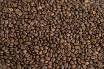 Dark roasted coffee beans are spread out on surface, showcasing their rich brown color and textured background. This display highlights the quality and variety of arabica or robusta beans. Copy space.