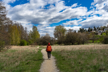 Woman tourist traveler with backpack walks through forest lake shore in nature spring. Trekking hiking trips tourism. Back view. Scandinavia paths trails. Active lifestyle. Sports recreation holidays.