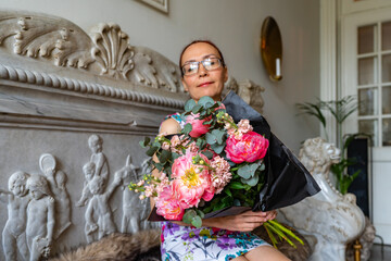Big beautiful bouquet lots of flowers is held by a middle aged woman. Focus on the bouquet. Lady female with flowers in beautiful antique interiors. 