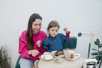 Mother and daughter in a cafe, drinking coffee and cocoa, eating a croissant and cake. Having fun...