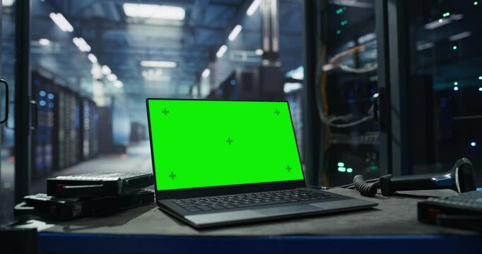 Laptop Computer with Green Screen Mock Up Display Standing on a Pushcart in a Technological Data Center with Server Cabinets. Table with Storage Hard Drives, Equipment, Computer and Scanner Device